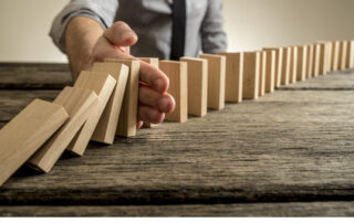 Ein Mann stoppt den Dominoeffekt einer Dominoreihe mit der Hand.