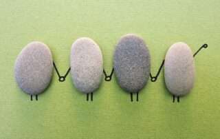 Vier ovale, flache Steine mit angemalten Händen und Beinen, die eine horizontale Kette bilden.