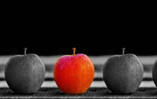 Fünf Äpfel in einer Reihe von denen nur der in der Mitte farbig ist, alles andere im Bild ist schwarz-weiß.
