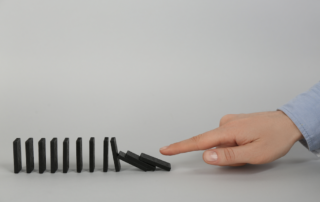 Eine Reihe Dominosteine die fallen und eine Hand die diese angestapft hat.