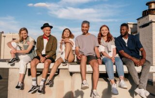 Eine diverse Gruppe von Menschen sitzen auf einer Dachkante und lachen.