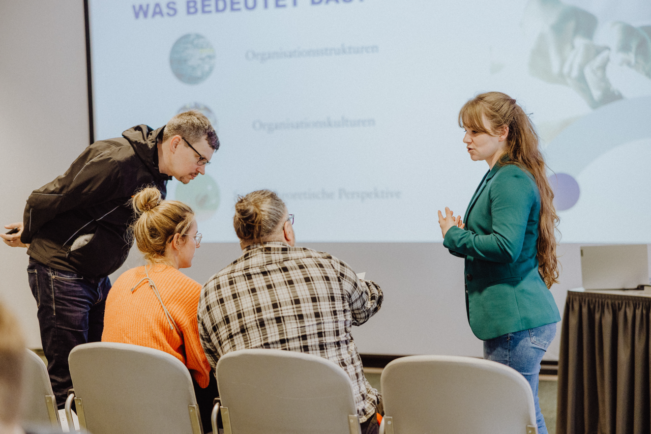 Gespräch mit vier Personen, drei stehen/sitzen nebeneinander eine Person steht gegenüber